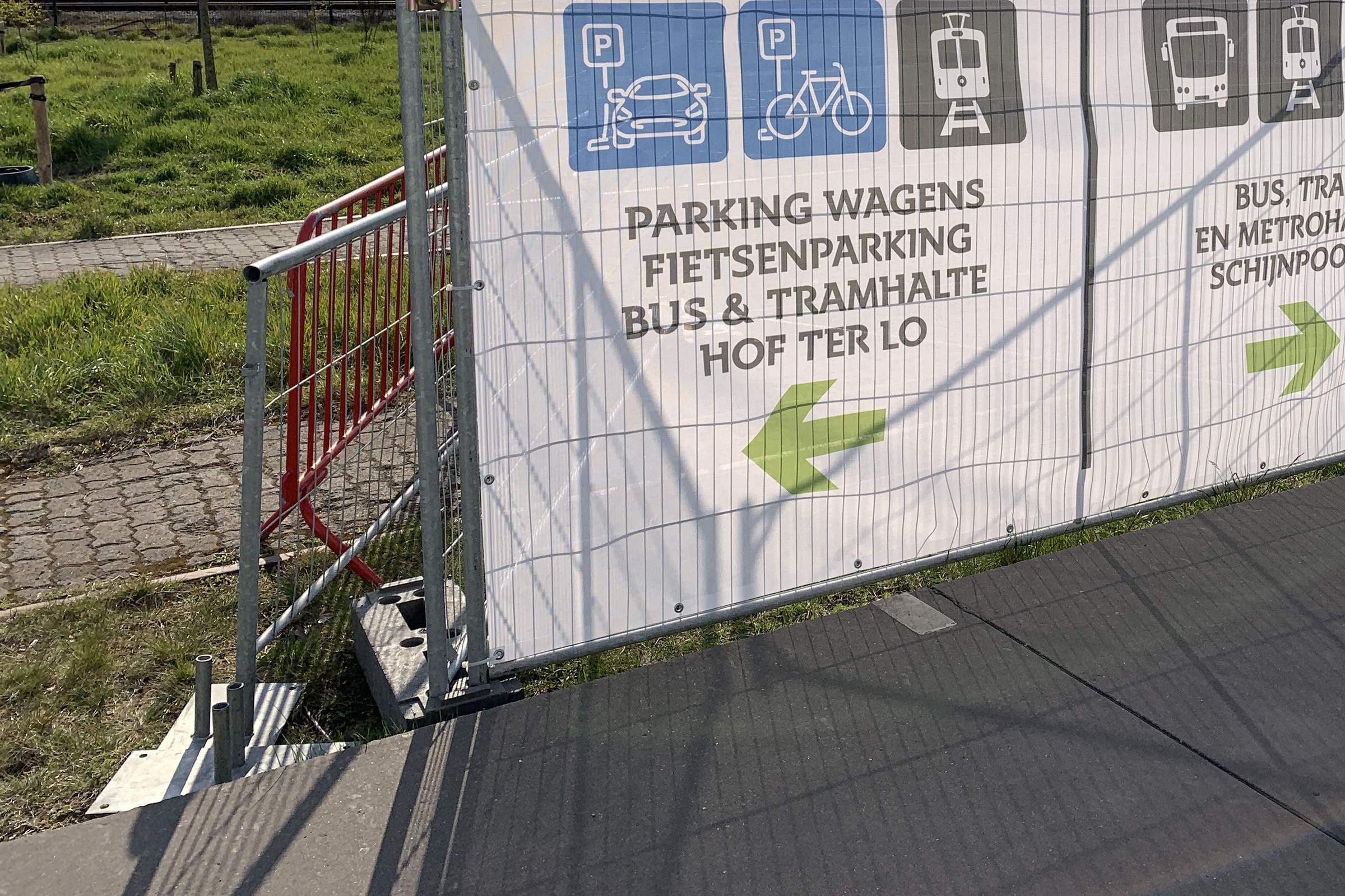 Werfhekken met wegwijzers naar parking, fietsenstalling en tramhalte bij een bouwproject