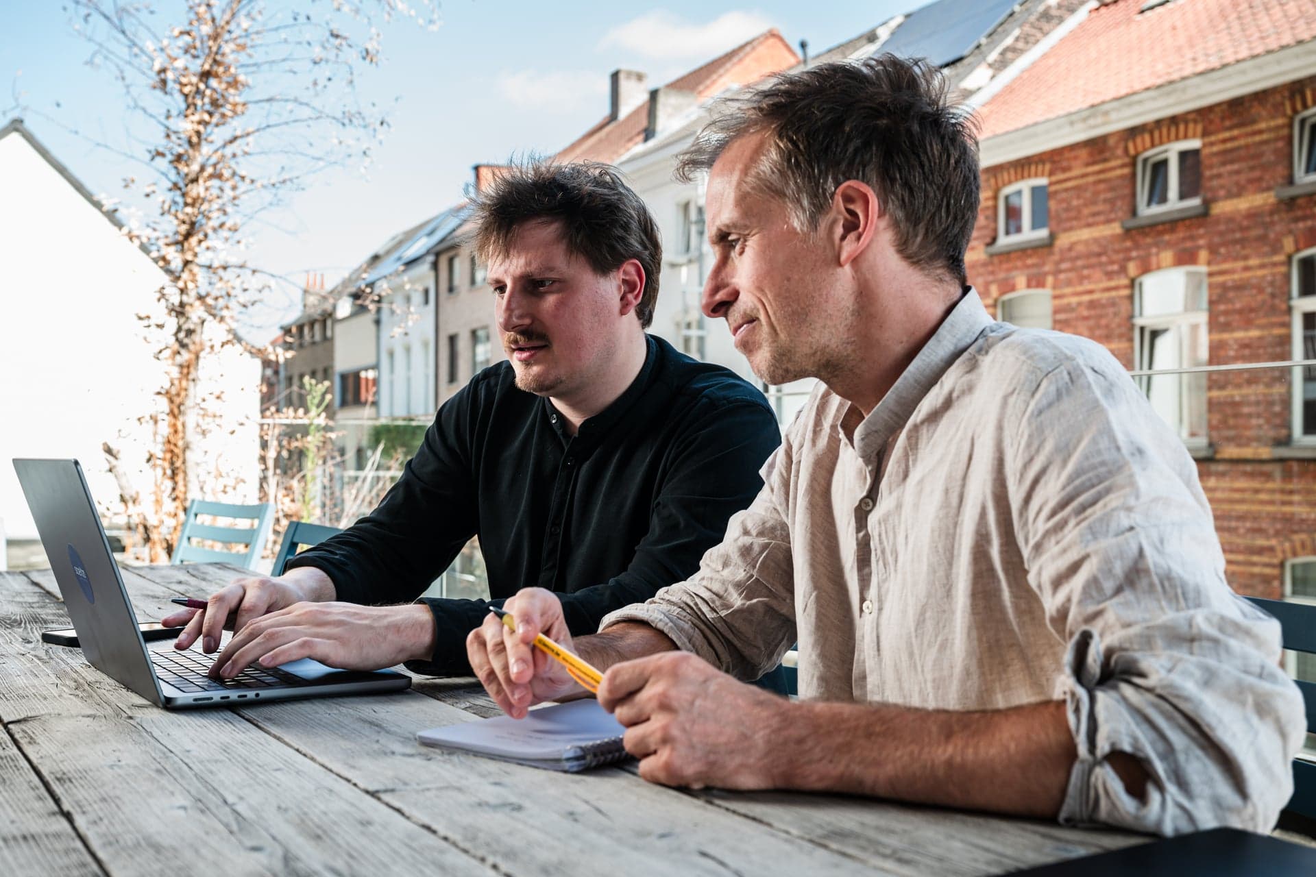 Twee collega’s van Scelta werken samen aan een laptop op een terras