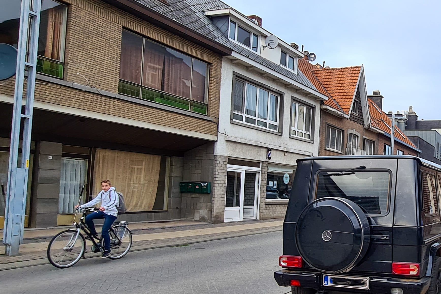 Een straat in een dorpskern met een fietser, geparkeerde auto’s en voetgangers