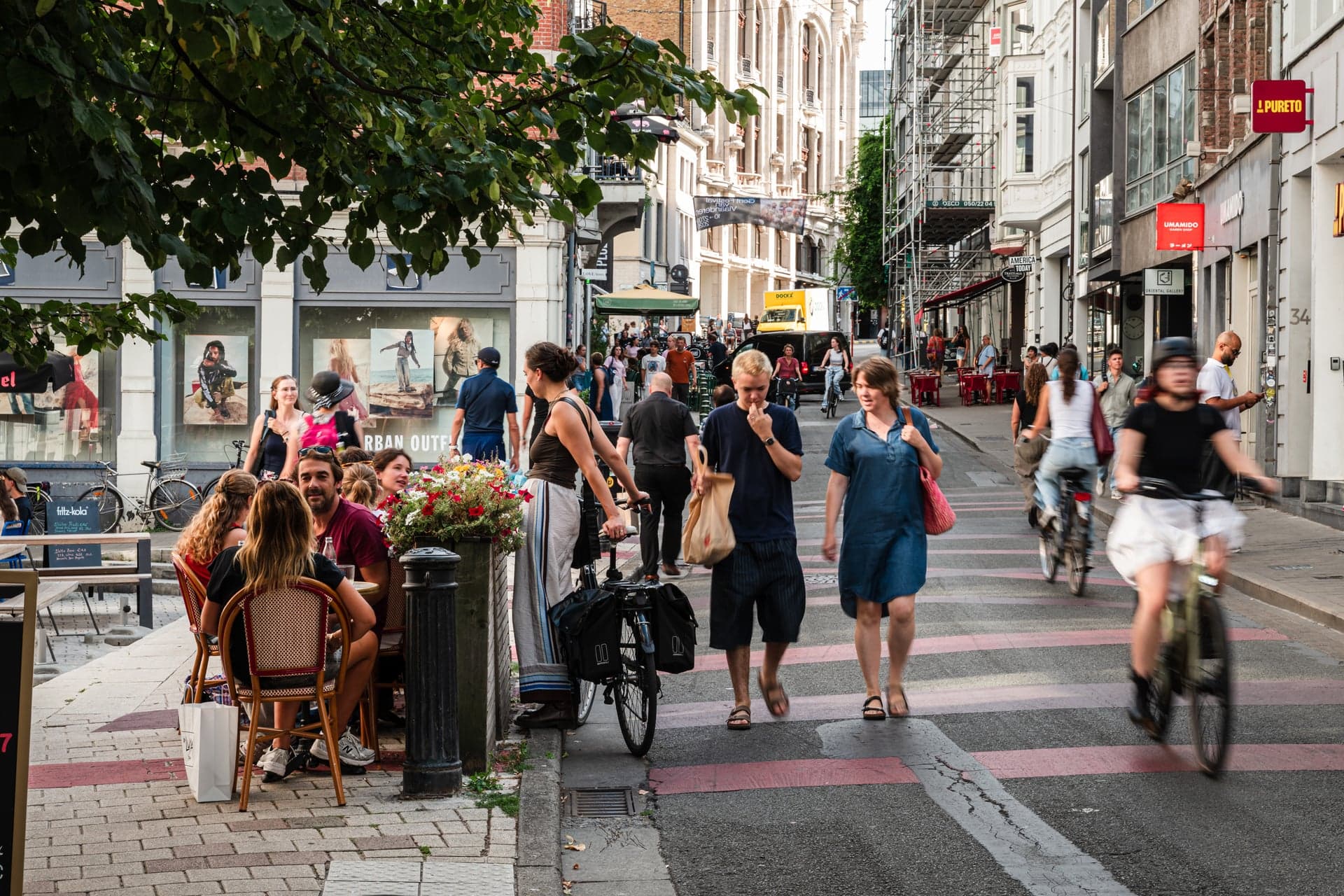 Een levendige winkelstraat met voetgangers, fietsers en een terras
