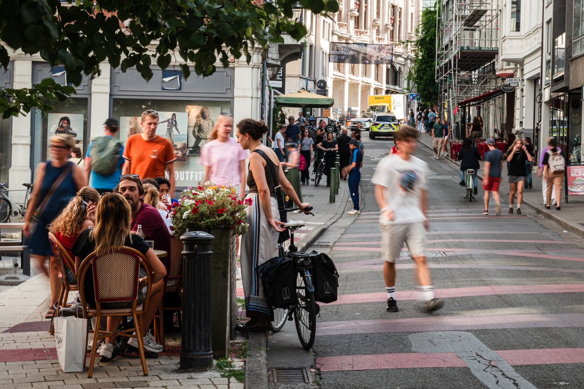 Een levendige winkelstraat met voetgangers, fietsers en terrasjes