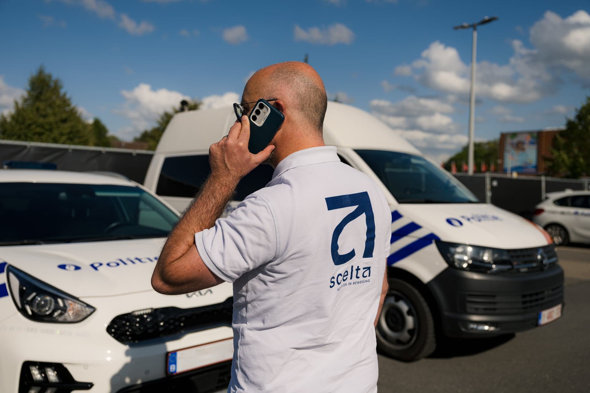 Een medewerker van Scelta overlegt telefonisch naast een politievoertuig